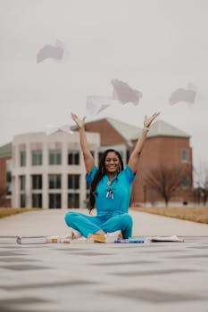 Happy medical student in blue scrubs celebrates graduation by tossing papers outdoors.